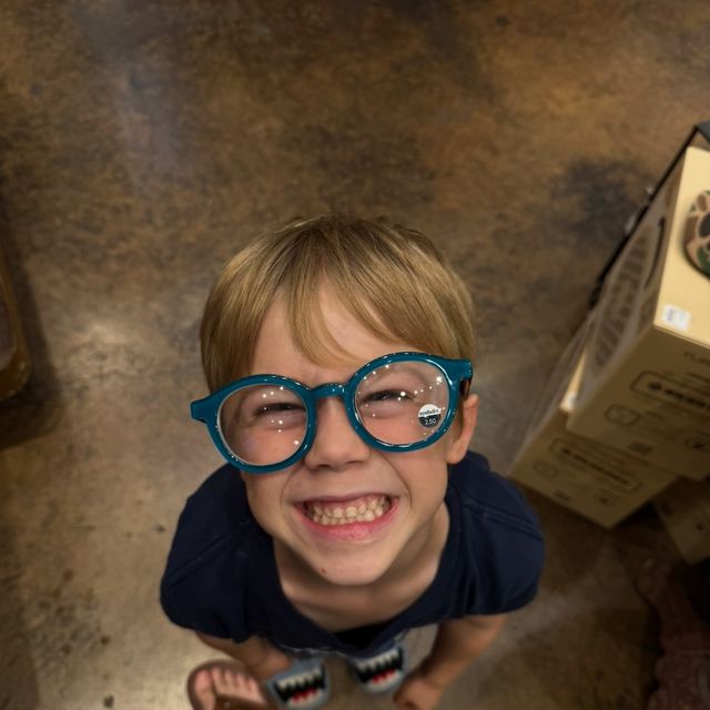Grayscale photo of a grinning kid in oversized teal glasses